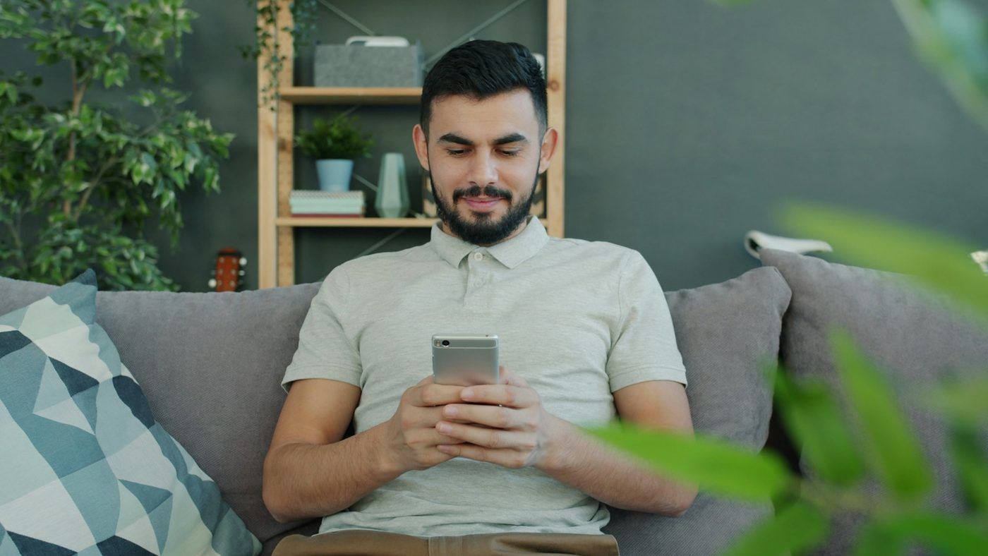 Ung mann i sofaen som blar på mobilen