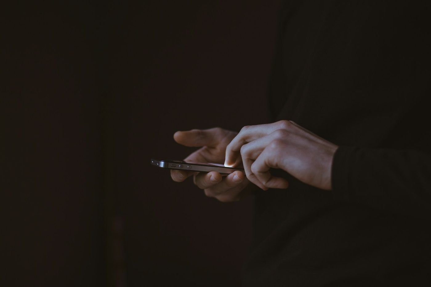 Hender som holder en mobiltelefon i mørket
